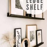 shows another angle of the dark stained ledge shelves with upcycle frames on a gray wall in a hallway with overlay text that says picture ledge shelf