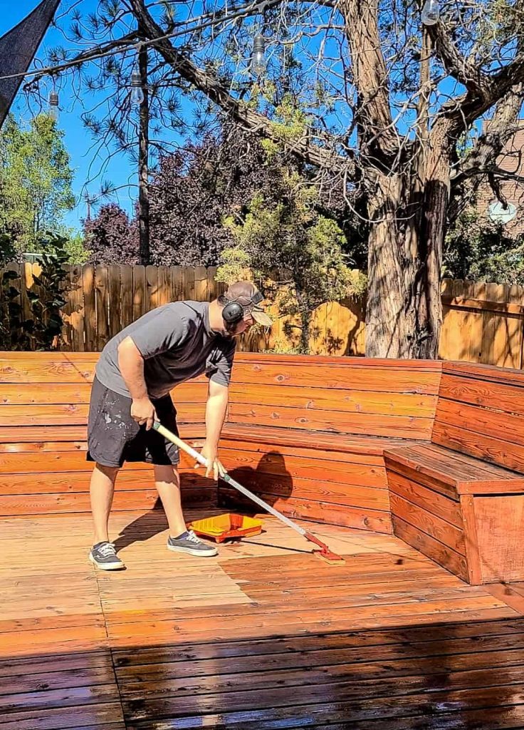 Man applying decking oil to wood deck using a sponge mop oil applicator.