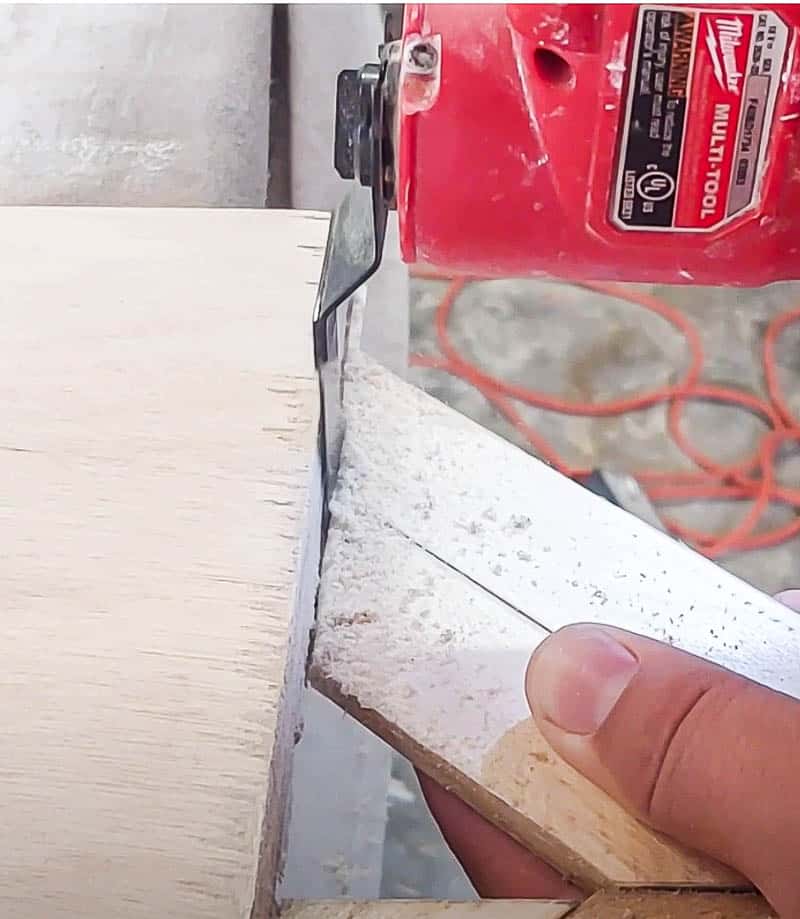shows a multi-tool trimming the edges of the wood shims overhang along the edge of the plywood on DIY wood wall decor piece