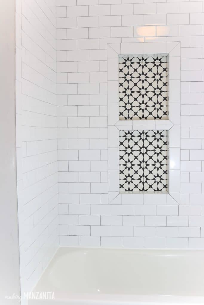 This bathroom shower is tiled with white subway tile, and decorative black and white cement tile in the background of the shower niche.