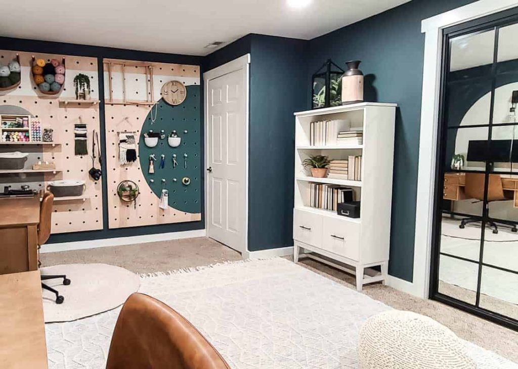 shows the other corner of the office with dark green walls, white book case with filing drawers and a giant wood pegboard to hold craft and art supplies 