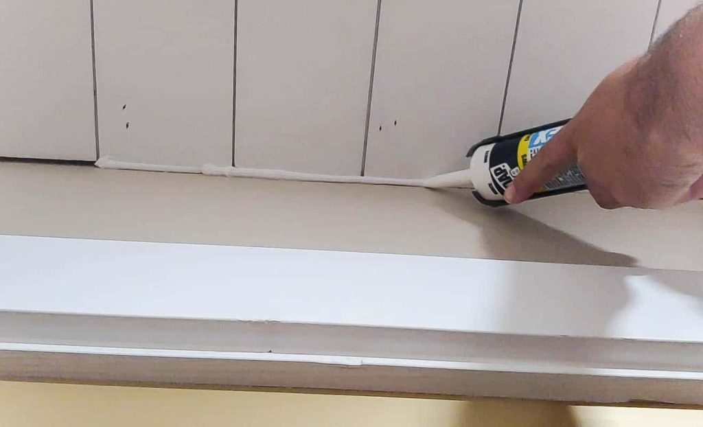 Using caulk to seal the space between the wall and shiplap ceiling planks