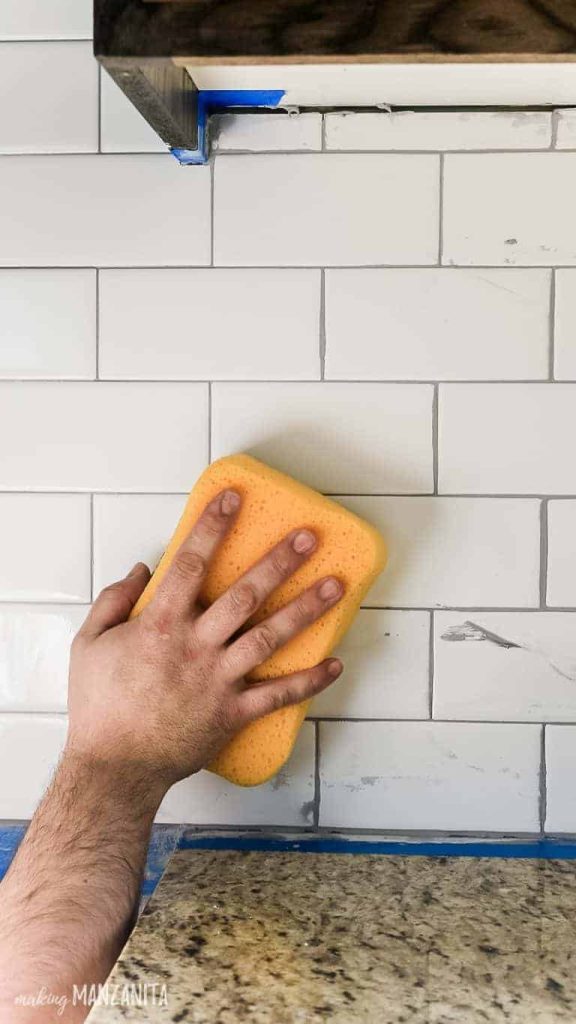 Using a large sponge to clean grout off of our white subway tile kitchen backsplash.