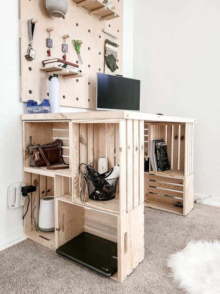 shows angled view of DIY wood crate desk with a computer and wood pegboard wall above it