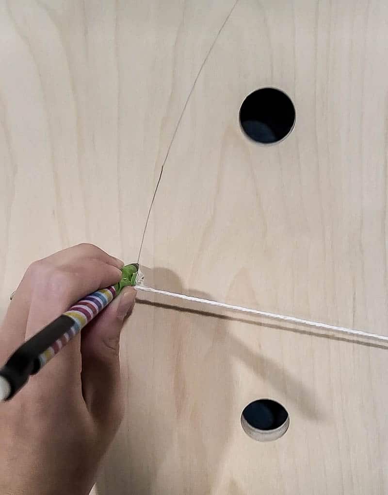 Using string and a pencil to create a circle stencil on the bare pegboard wood, creating a desing.