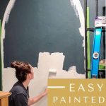 Woman using a 4 inch roller to paint a tan arch shape on the wall with text overlay that says easy painted arch accent wall