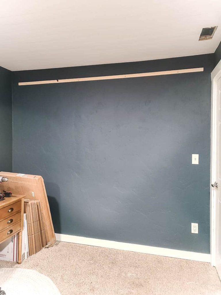 A blank wall, painted with a dark navy paint color, and one installed french cleat, where our giant pegboard wall will hang.