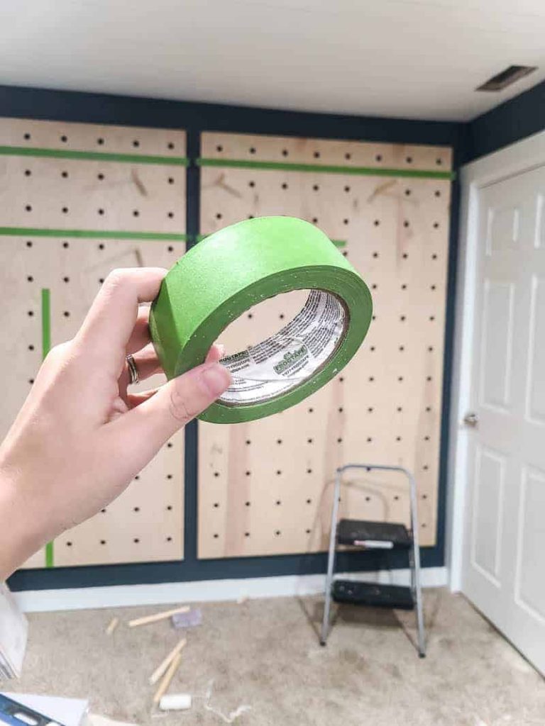 Holding up a roll of frog tape - the best tool for painting clean lines and sections - in front of our hanging giant pegboard wall.