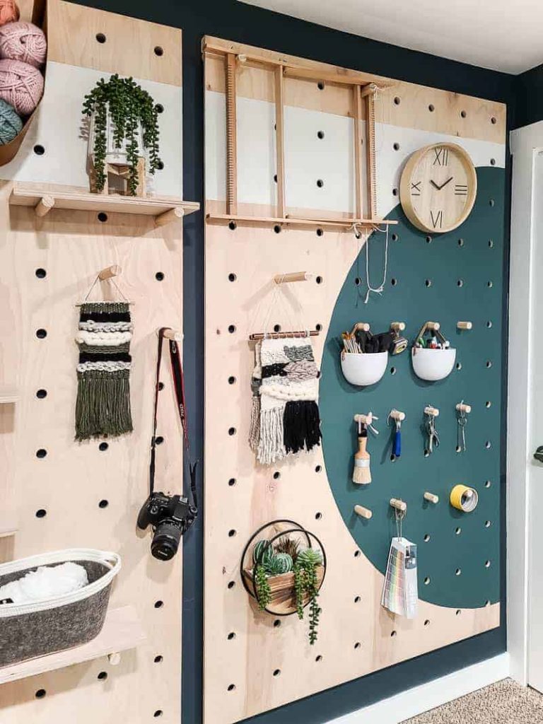 Our completed giant pegboard wall hangs with neatly organized and styled crafting supplies hanging from dowel rods.