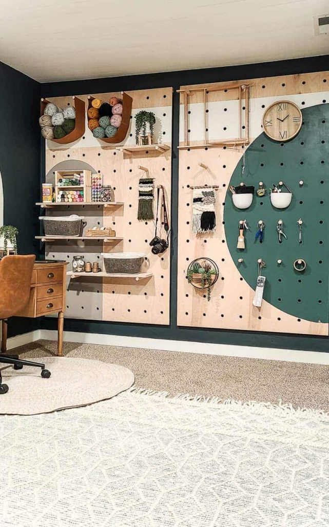 shows the dark teal wall with a wood pegboard with painted shapes with multiple craft supplies