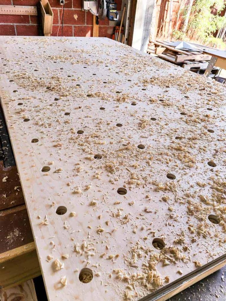 Our giant pegboard wall is in progress! The plywood has large holes drilled through, with sawdust spread over the surface.