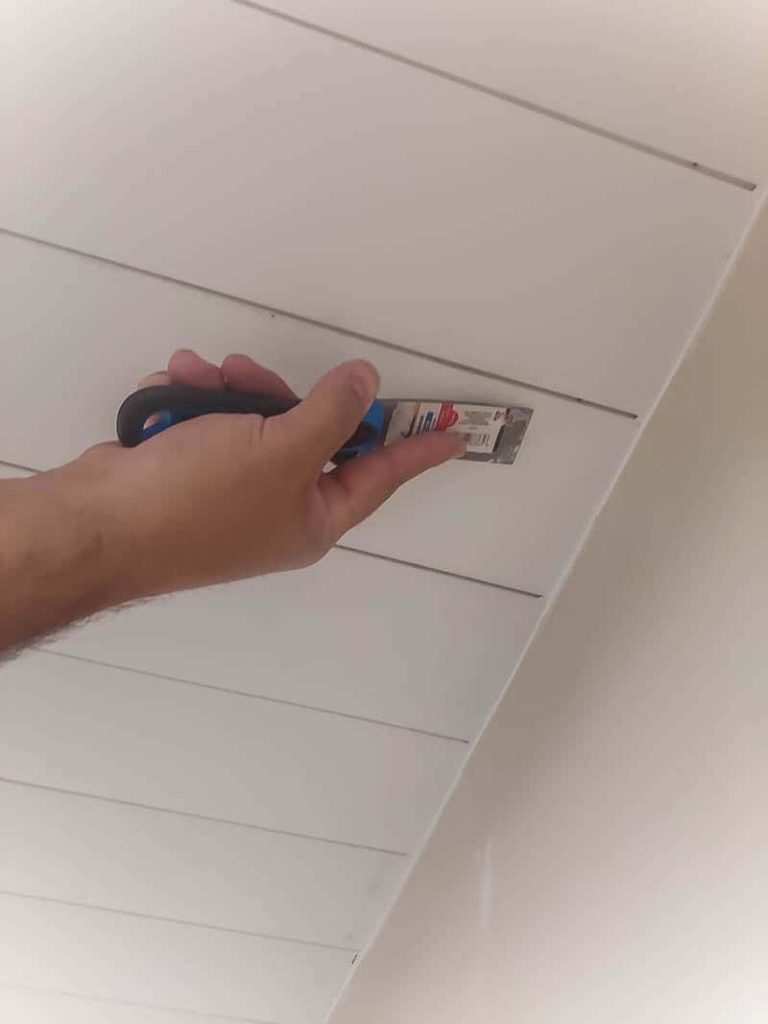 Using a putty knife to smooth spackle over nail holes in the newly installed shiplap ceiling panels