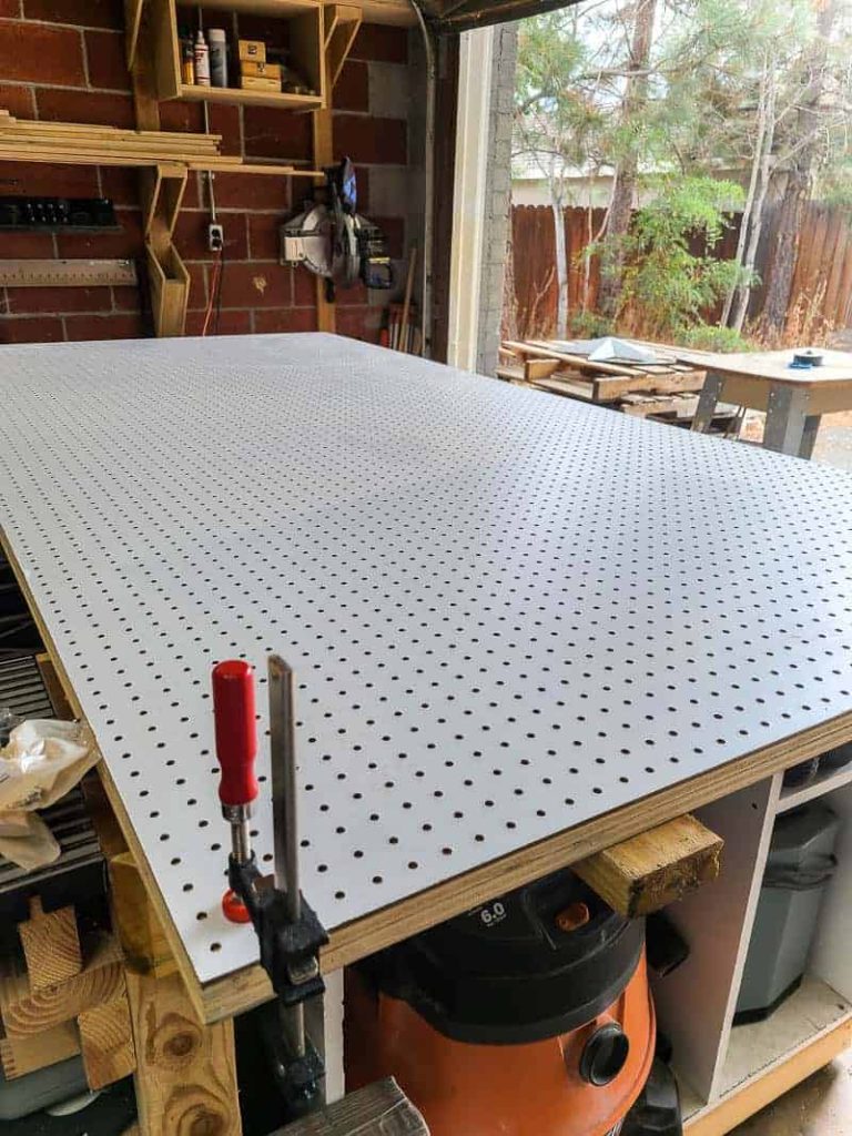 A large MDF pegboard panel lays on a workbench in the garage.