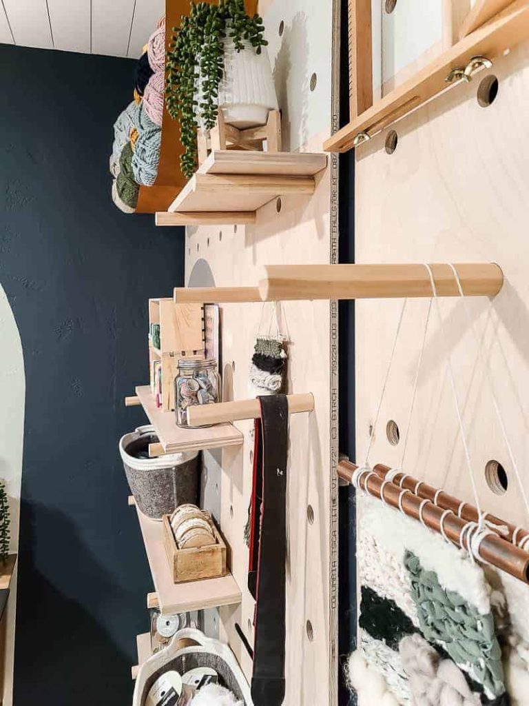 A closer look at our giant pegboard wall, with items hanging from dowel rods and shelves installed, holding various crafting supplies and other miscellaneous items.