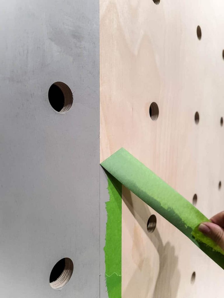 Removing painters tape from our freshly painted pegboard wall.