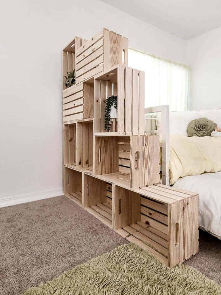 shows a side view of the wood crate bookshelf by a bed and with plants in it