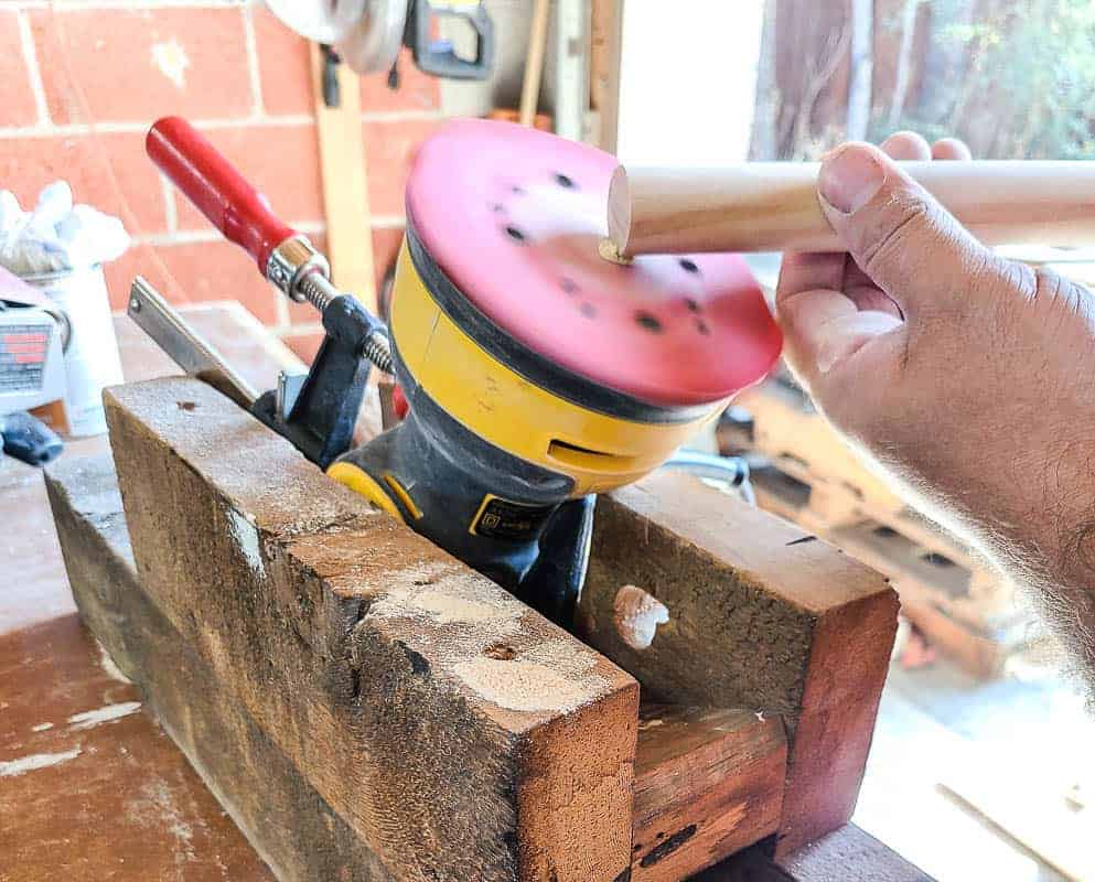 Using an orbital sander to sand smooth the cut edges of the dowel rods for our giant pegboard wall.