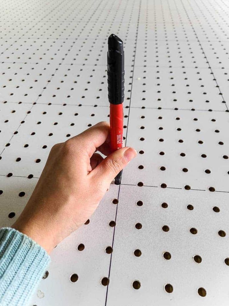 Using a sharpie marker to mark pegboard holes, where we will drill and insert dowel rods.