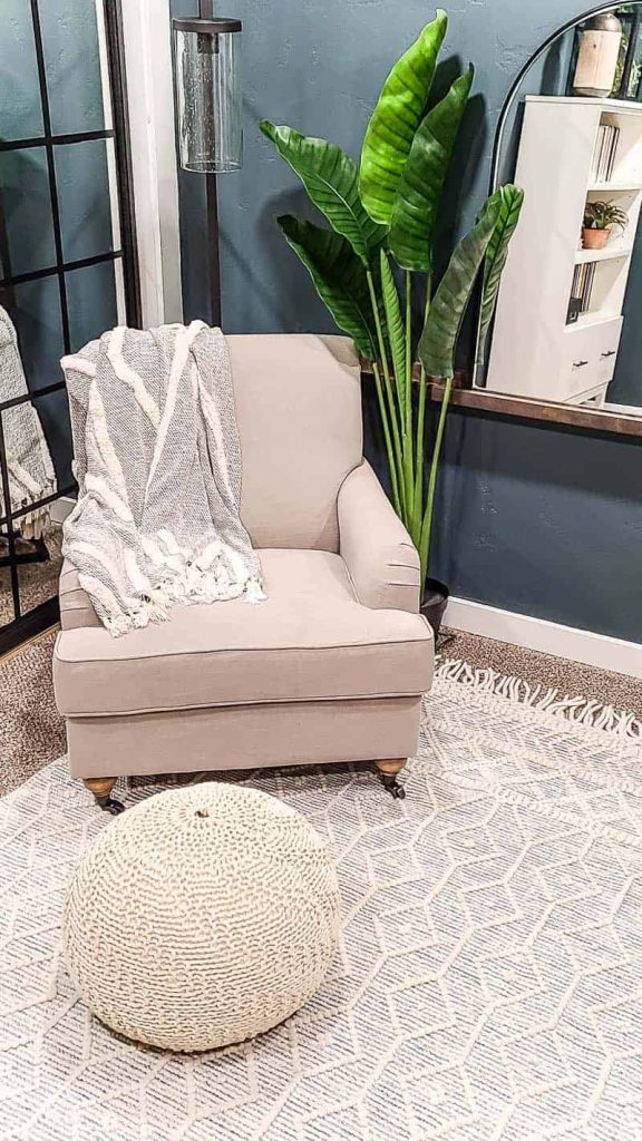 shows a corner of the dark teal office with a cream linen arm chair and faux plant, arch mirror on shelf and white boho rug