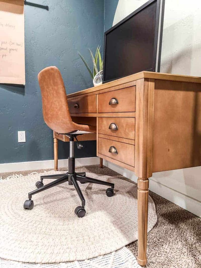 shows a wood desk with vintage brass pulls with a leather chair and white round rug