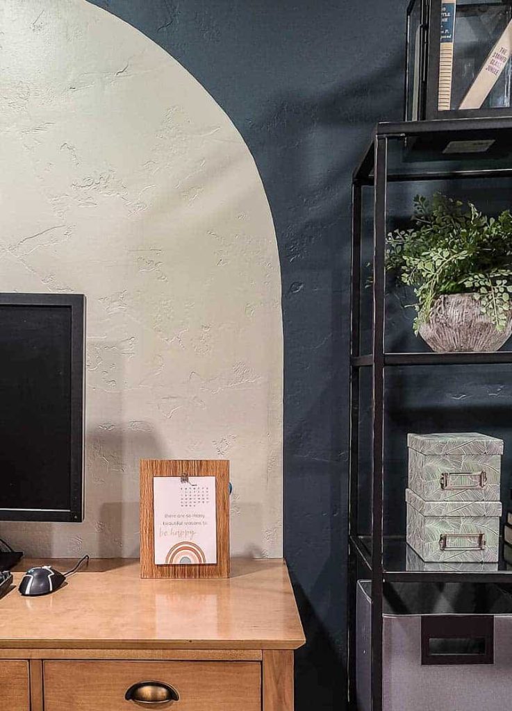An image of a desk and bookshelf in a home office, where a DIY wooden desk calendar sits on the desk next to a computer.