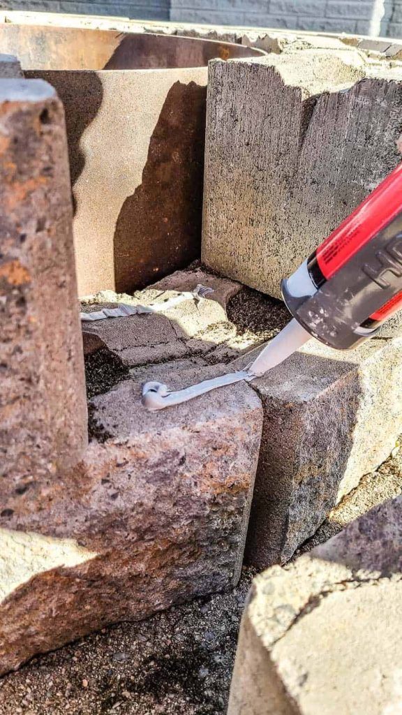 shows landscaping adhesive between layers of wall blocks for round fire pit