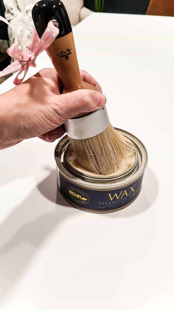 A large, round paint brush dipping into a can of Behr wax decorative finish.