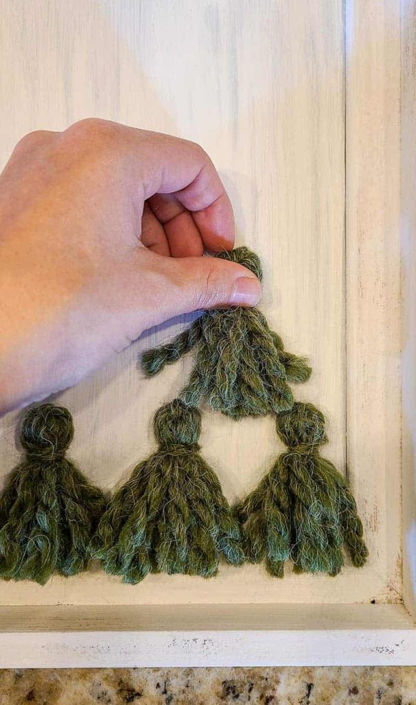 Applying small green Christmas tree tassels to frame