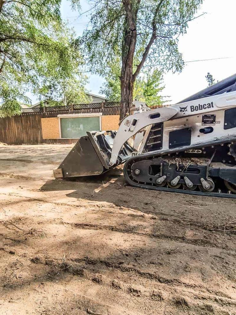 shows a bobcat skid steer leveling out dirt in backyard for renovation