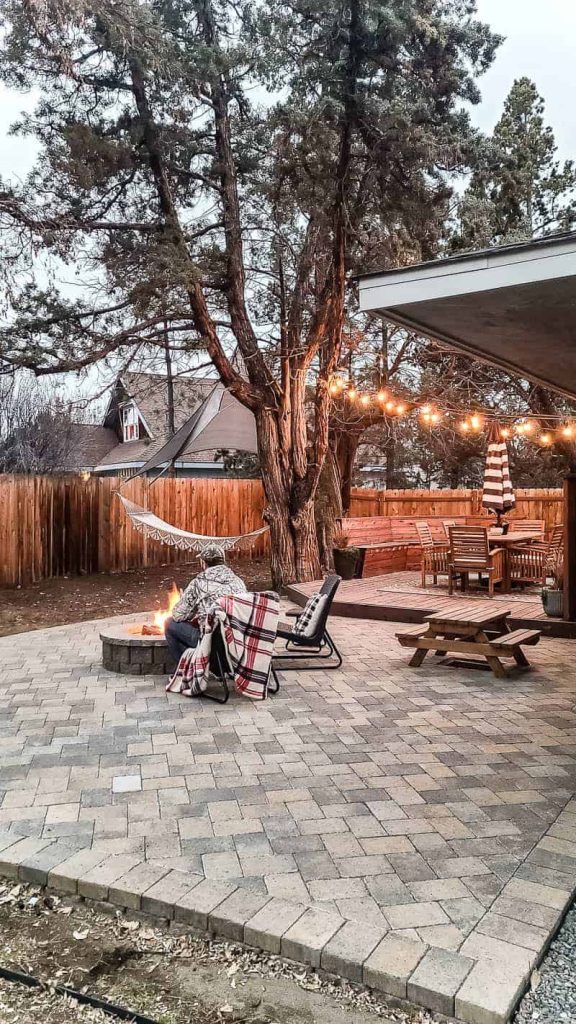 man sits in front of lit fire pit on paver patio