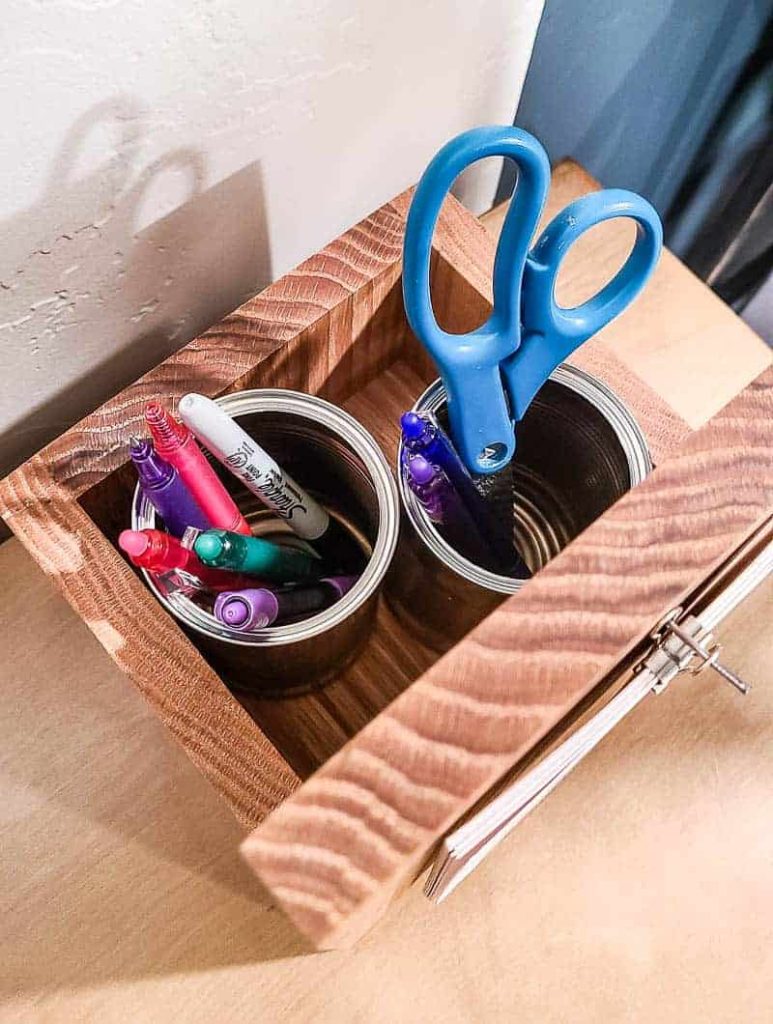 A close up image shows the back of the DIY wooden desk calendar, which contains a box that holds two aluminum jars to hold pens, markers, and scissors.