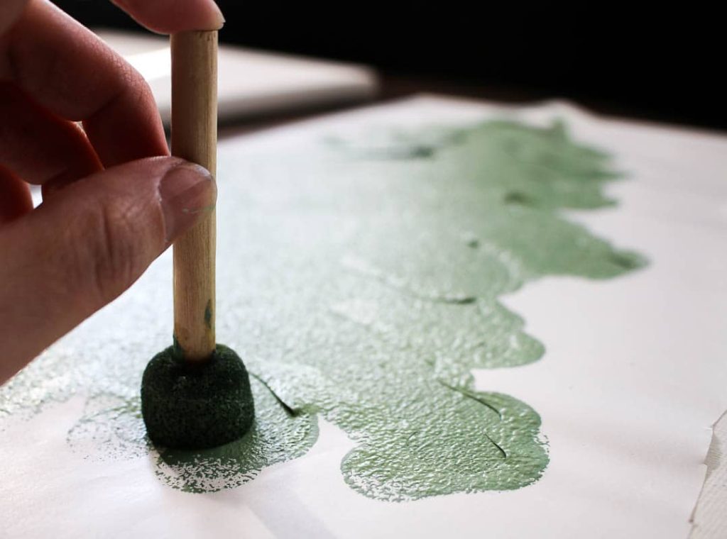 shows a hand painting a tree on a canvas with stencil