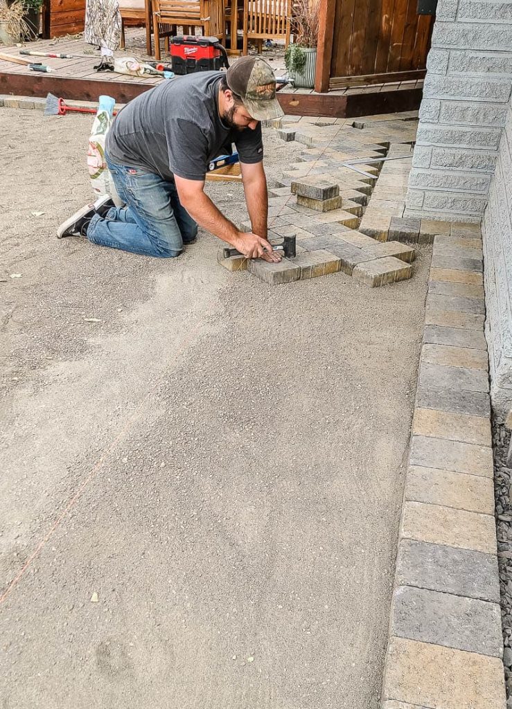 Man lays pavers in a row along one edge in a herringbone pattern