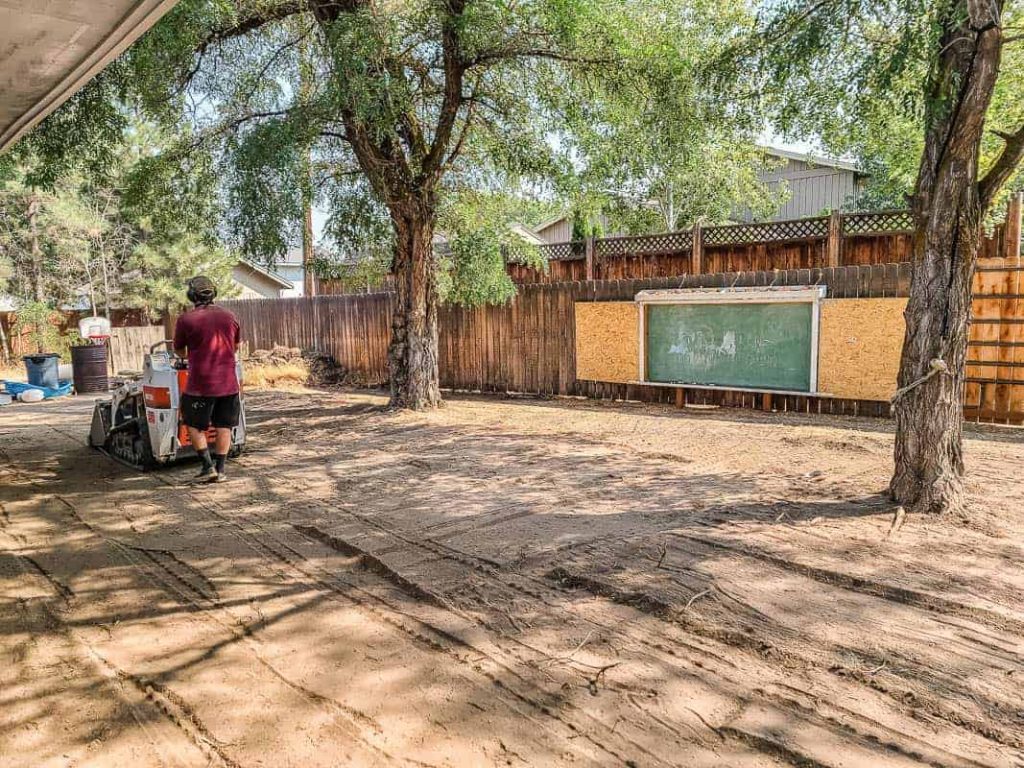 shows a man leveling out the dirt in a backyard