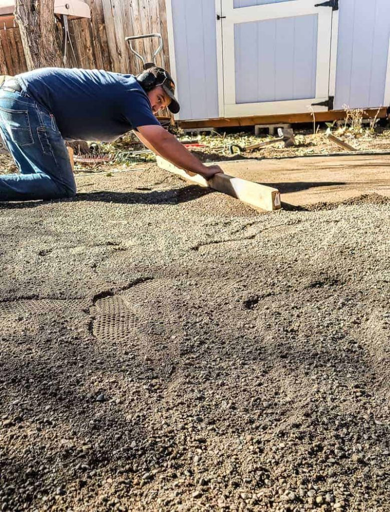 man uses two by four to level the paver base sand before adding a DIY paver patio with fire pit