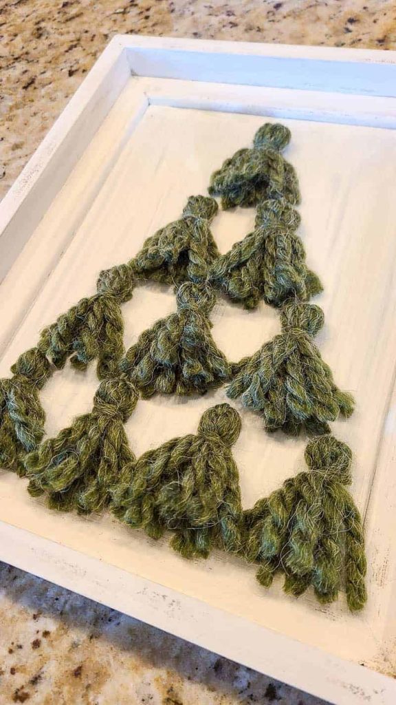 White frame with green yarn tassels in shape of Christmas tree