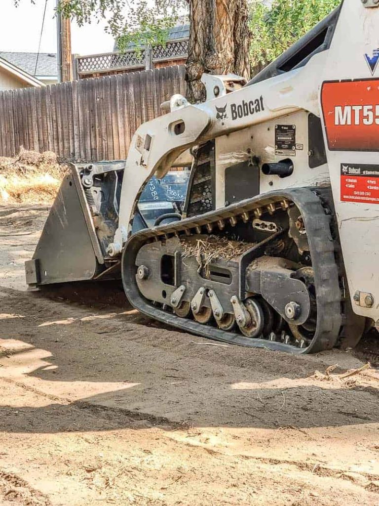 a bobcat tractor is flattening the dirt in backyard