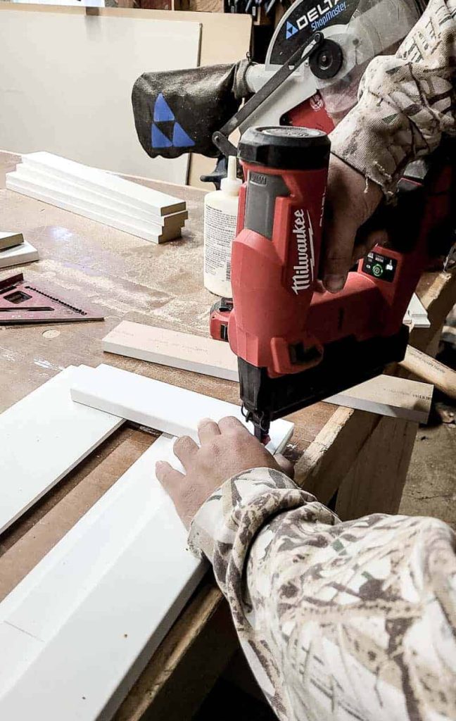 shows a man using a brad nailer to put the nails into the box
