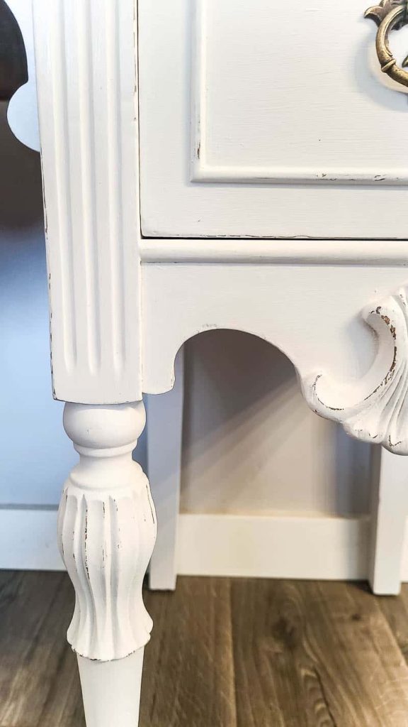 A close up look at the leg and details of the vintage wood desk, painted with white chalk paint, and distressed with a sander.