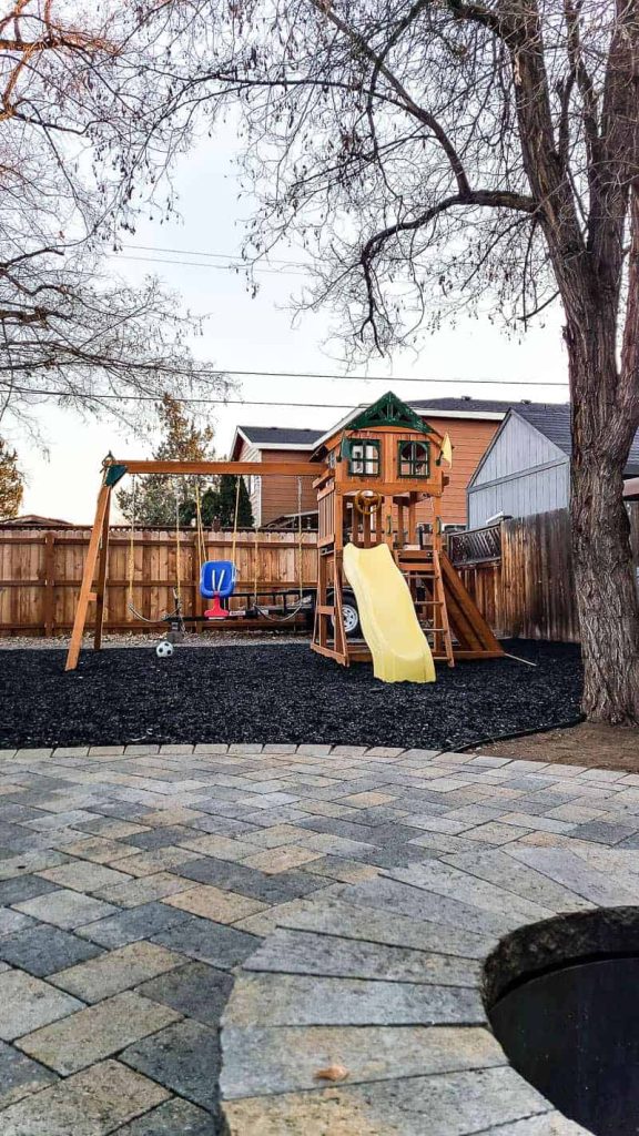 playground area with swing set in backyard with paver patio in foreground