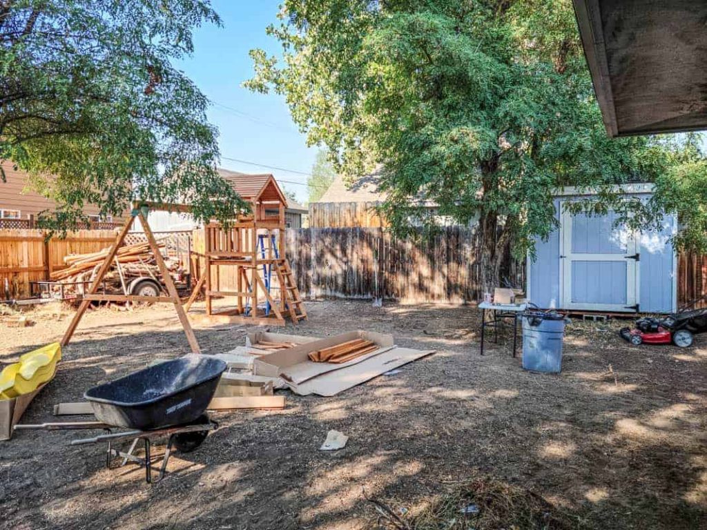 Wooden backyard playset with swings and slide getting assembled in backyard 