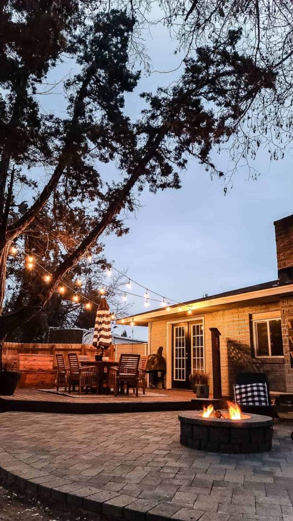 nighttime string lights illuminate the deck, and the fire pit lights up the patio