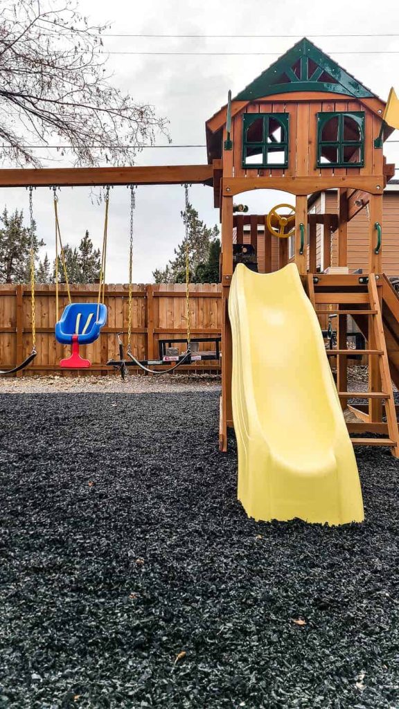 wooden Swing set on black rubber mulch with yellow slide