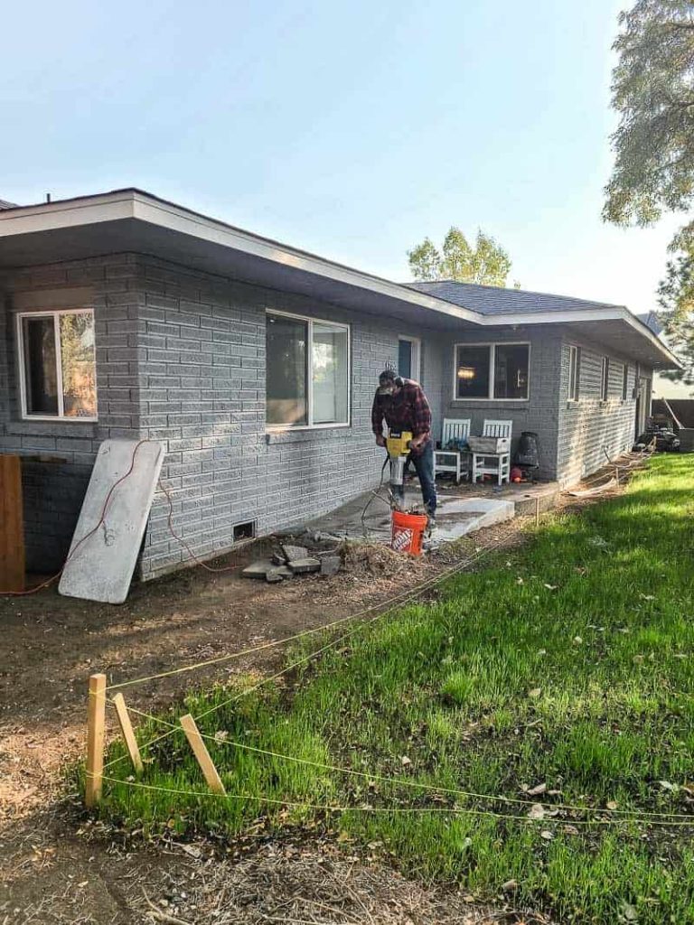 Man using jack hammer to remove concrete pad and ramp by backdoor in backyard during renovation