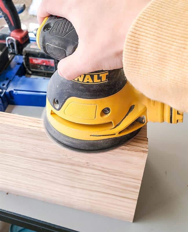The wood is being sanded using an orbital sander to create a smooth finish for a desk calendar and wooden pencil holder.