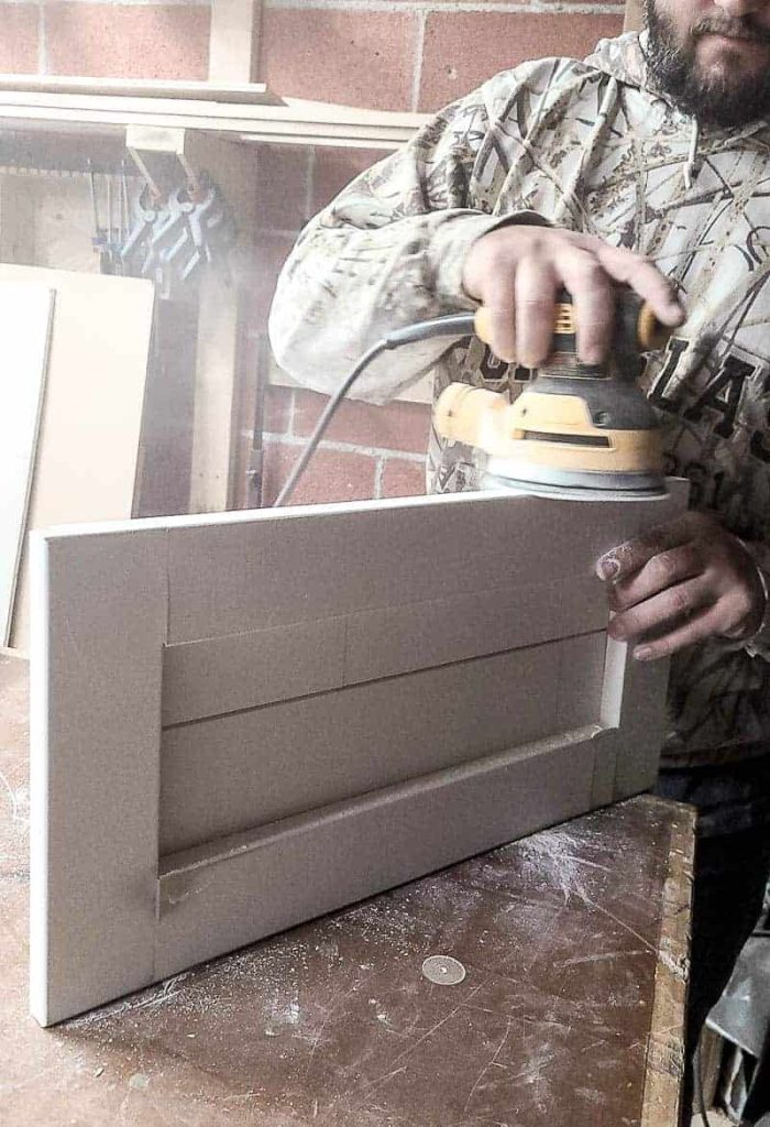 shows a man using a sander on the edge of the shiplap tree stand