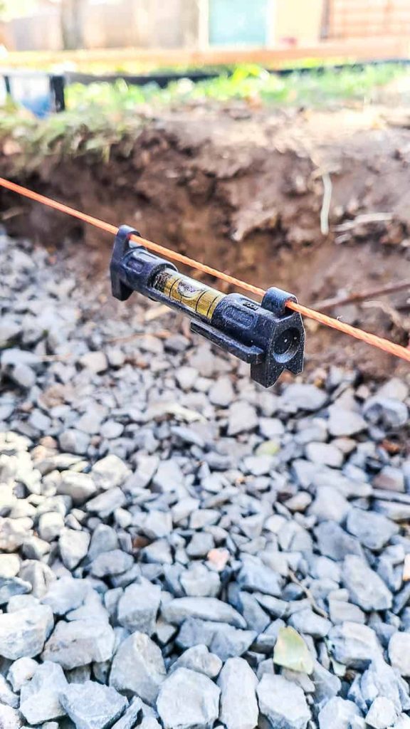 a level hangs on a string line with gravel trench in the background