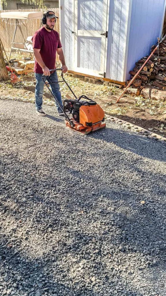 man uses a plate compactor on gravel base before installing a paver patio 