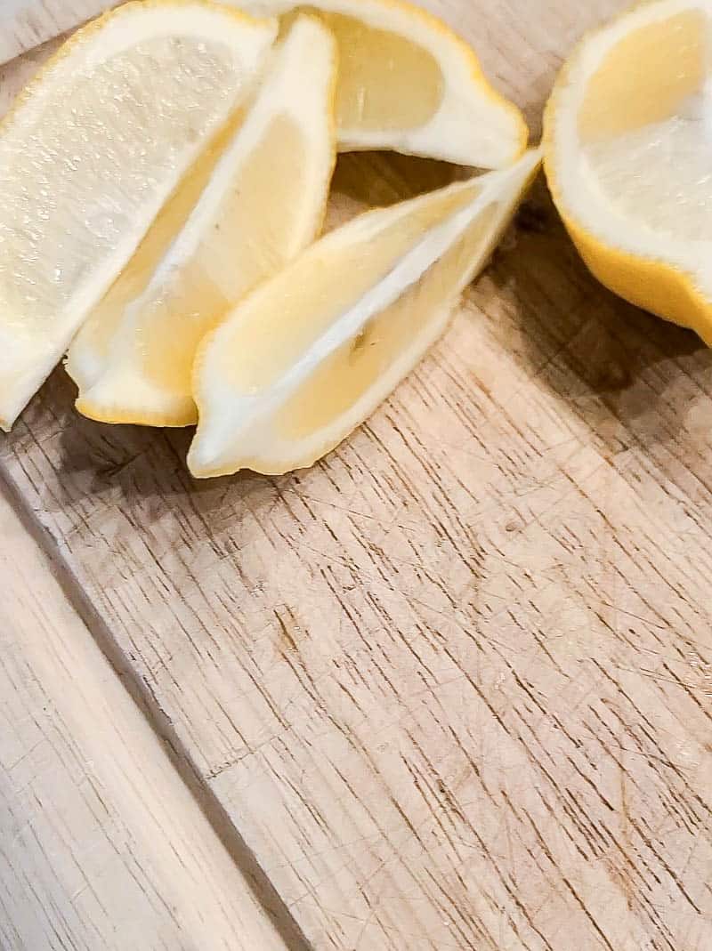 Sliced lemon wedges sit on a wooden cutting board.