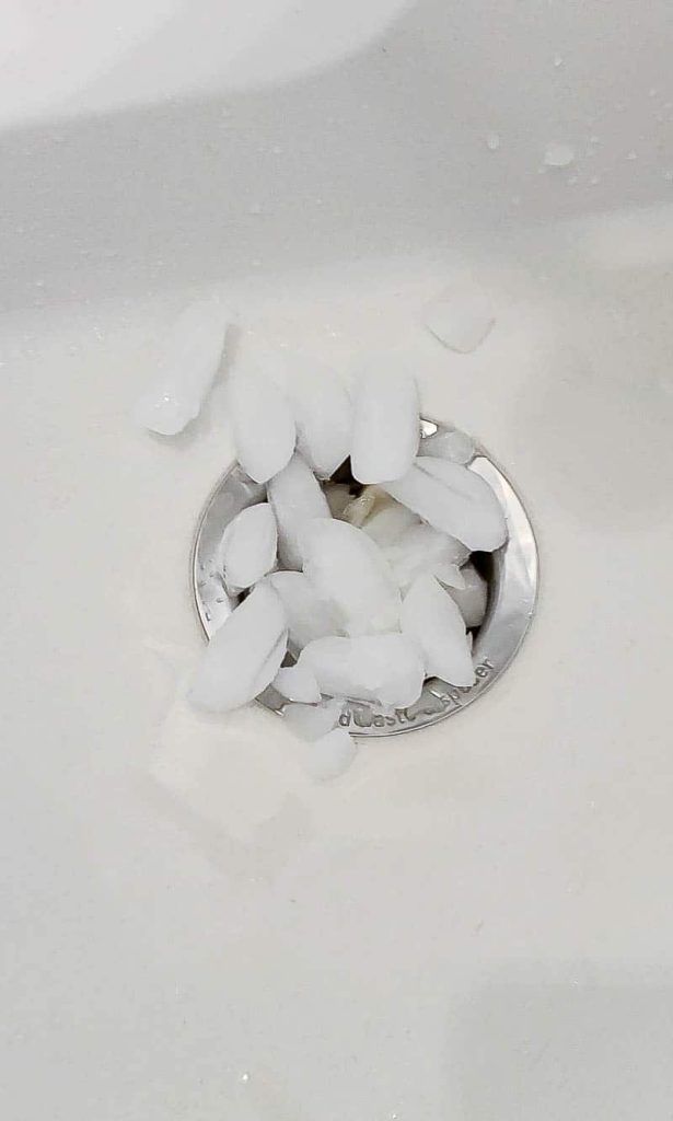 A pile of ice cubes sits in and around the drain of a garbage disposal in a white sink.